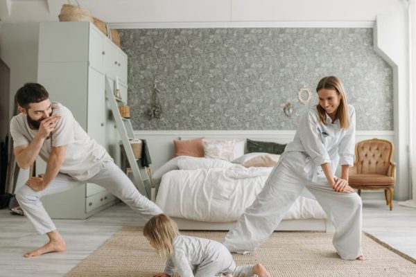 A joyful family bonding through morning stretches in a cozy bedroom setting.