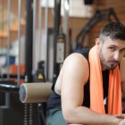 Adult male resting in a gym with an orange towel after strength training.