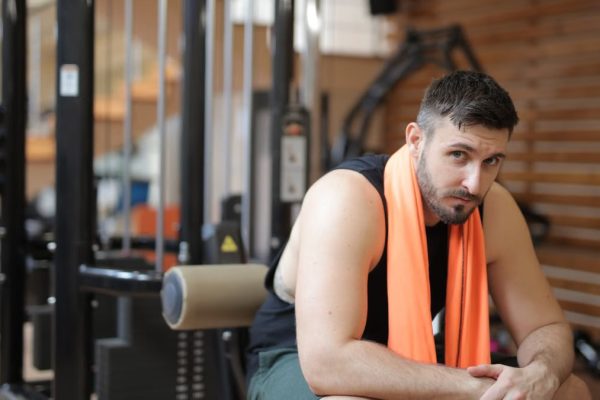 Adult male resting in a gym with an orange towel after strength training.