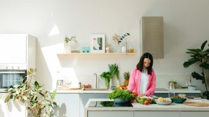 A woman in pink prepares fresh vegetables in a sunlit, modern kitchen, creating a vibrant cooking scene.