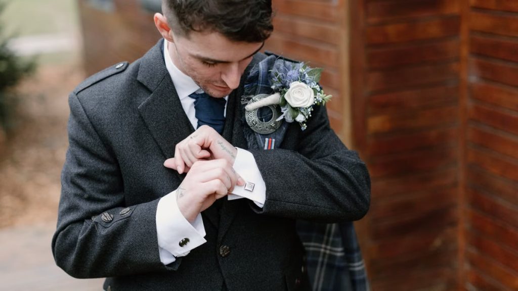 A groom in a suit adjusting cufflinks with a boutonniere on an elegant wedding day.